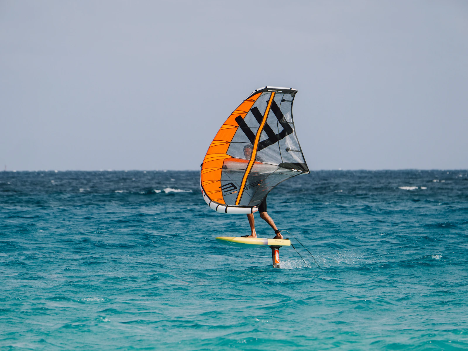 Navegante de wingfoil con vela naranja sobre agua azul